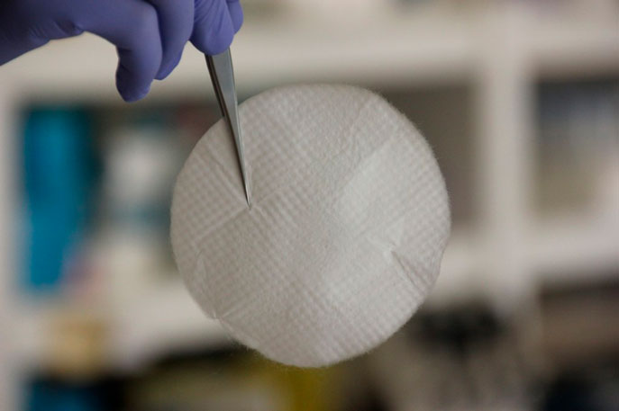 Membrana de nanofibras aguantada por dos pinzas que sujeta una mano con guantes quirúrgicos